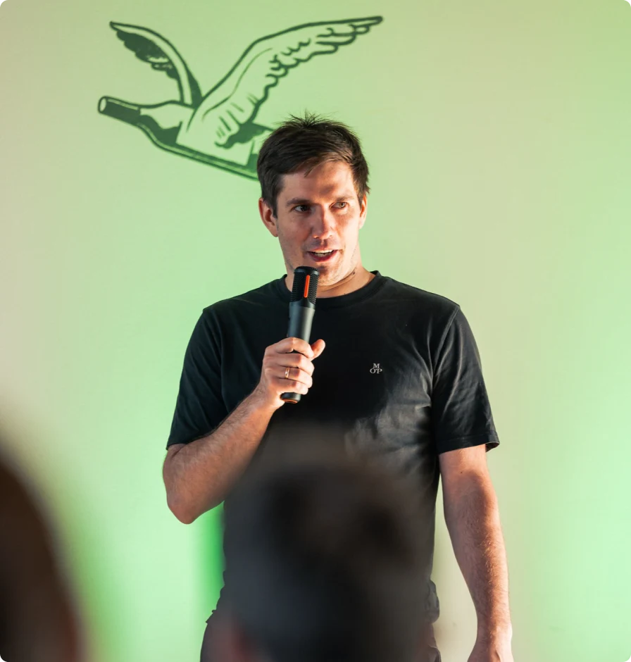 Arturs Kruze speaking into a microphone in front of a green wall.