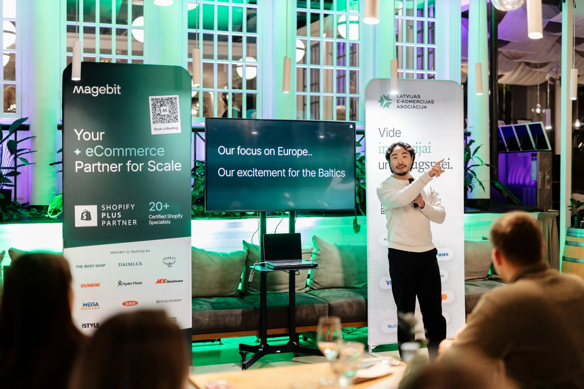 A Shopify speaker presenting Shopify's focus on Europe and the Baltics, between the Magebit and LATEKA banners at Kolonāde