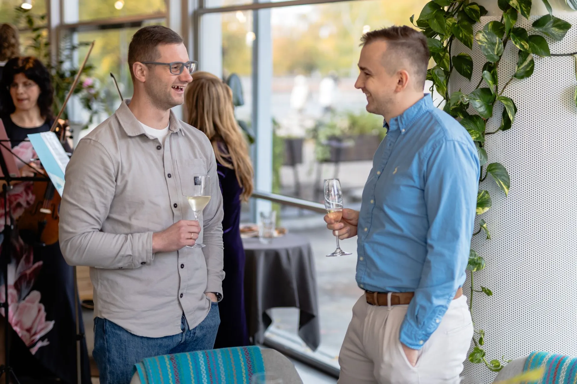Two guests talking with drinks by the window at Kolonāde