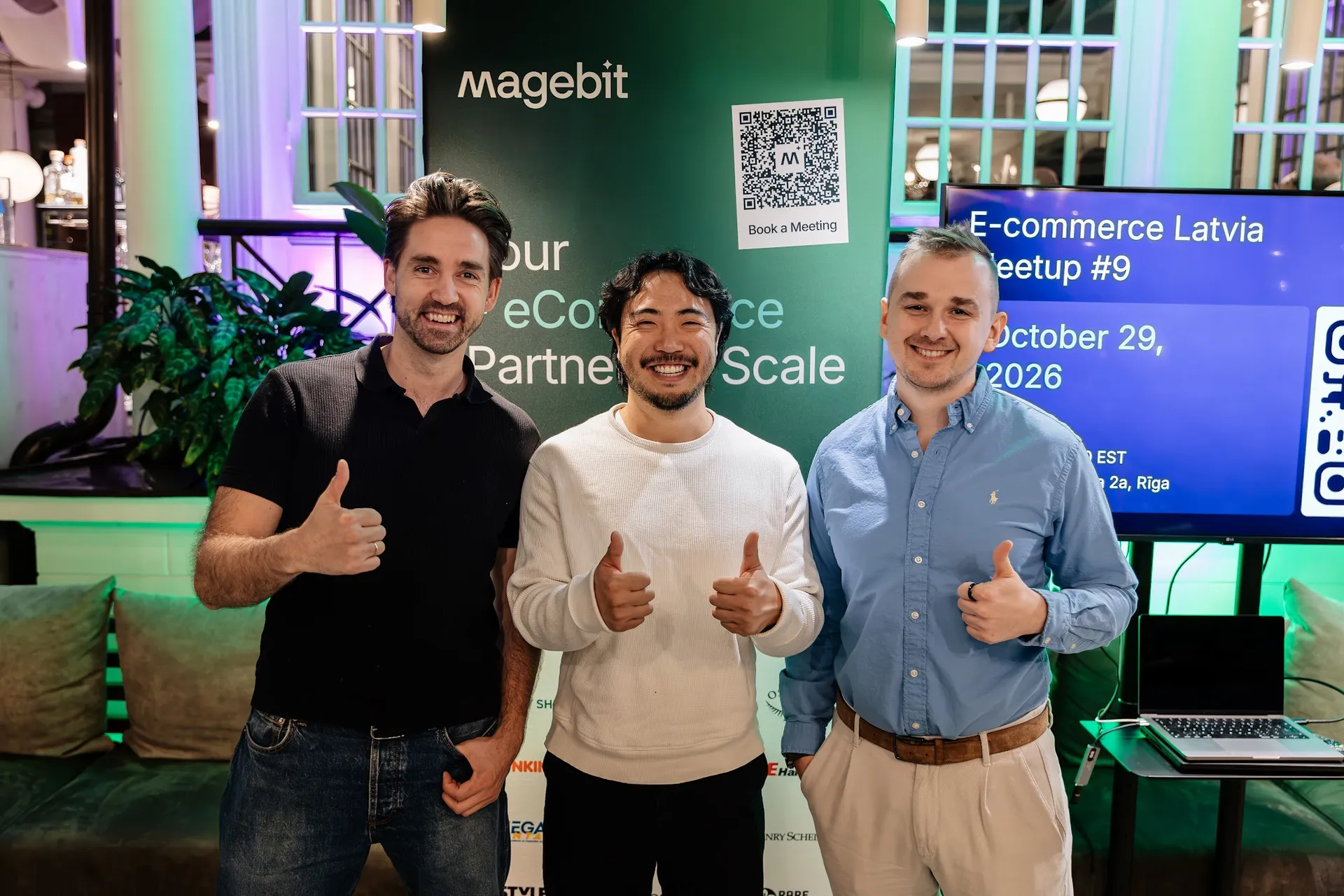 Three hosts giving a thumbs up in front of the Magebit banner at Kolonāde