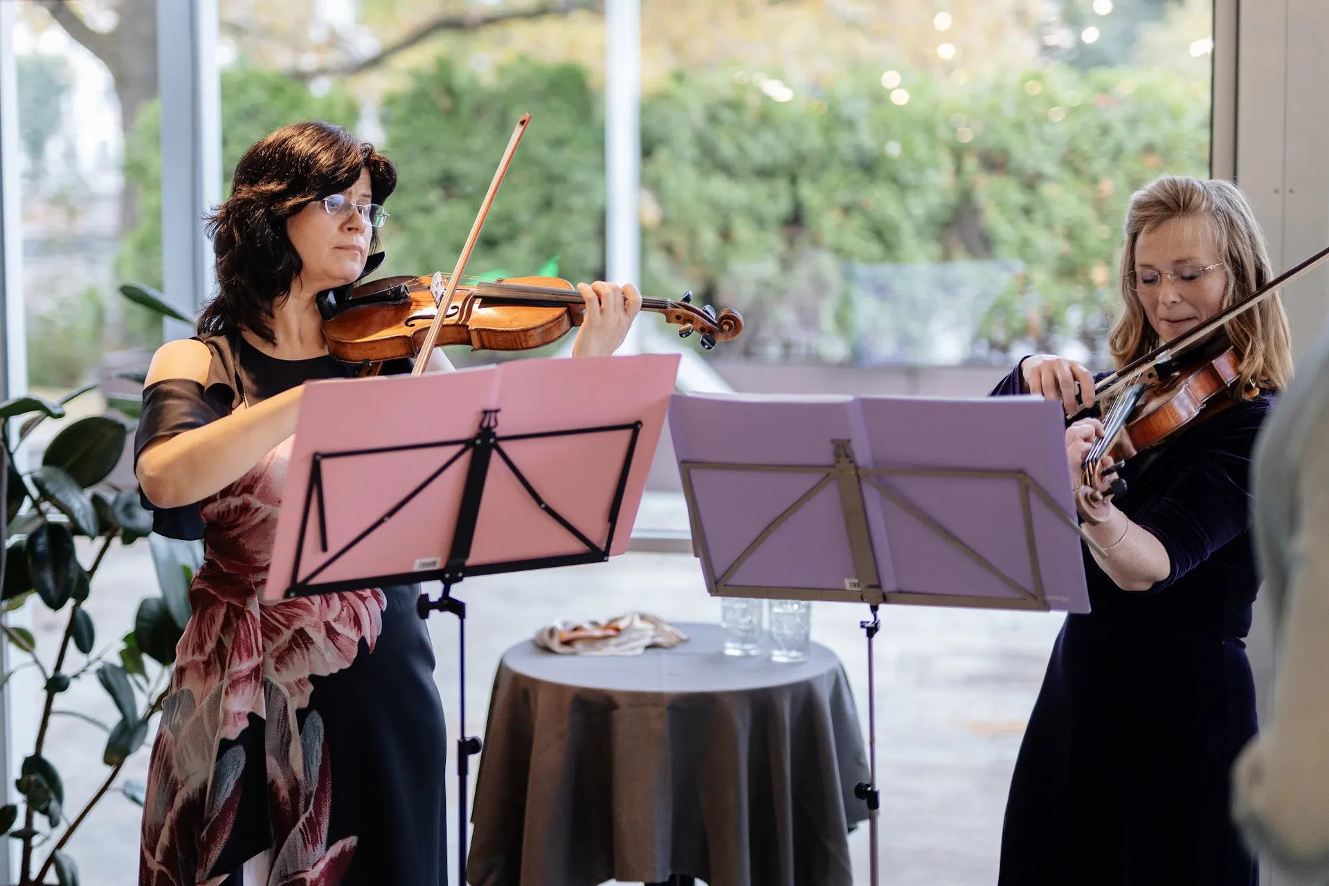 A string duo playing violin by the windows at Kolonāde during the welcome reception