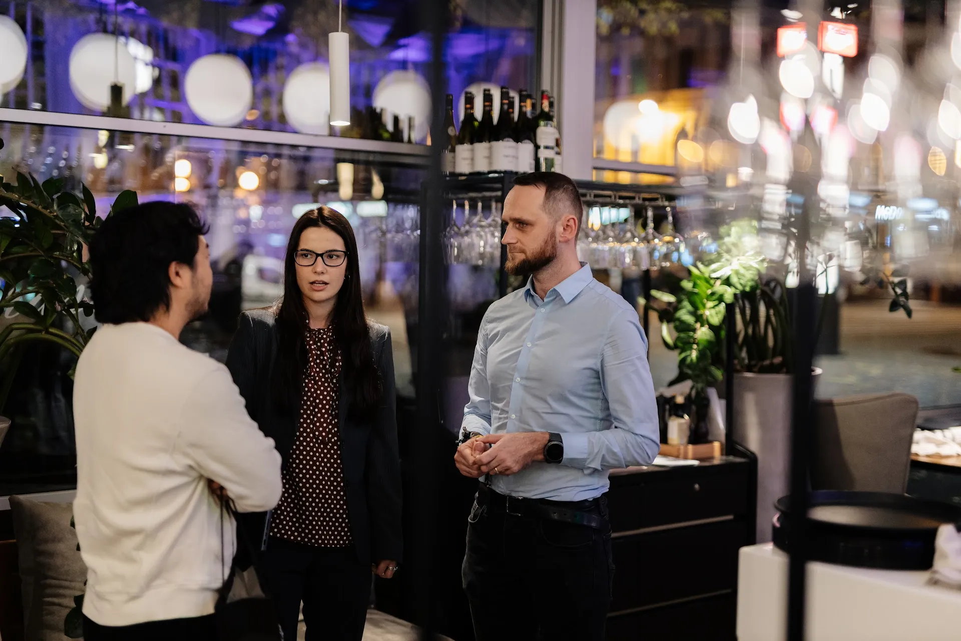Three guests in conversation by the bar at Kolonāde in the evening