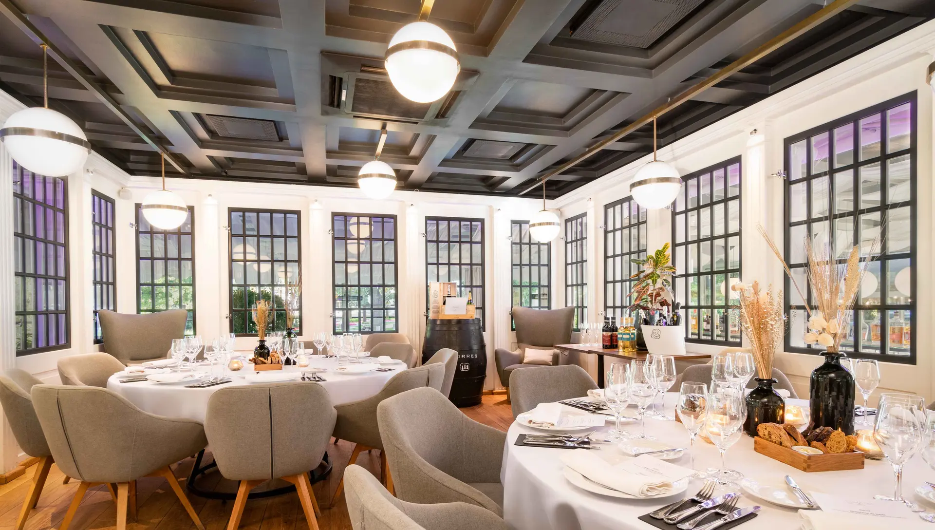 Dining room at Kolonāde with round tables set for dinner beneath tall windows