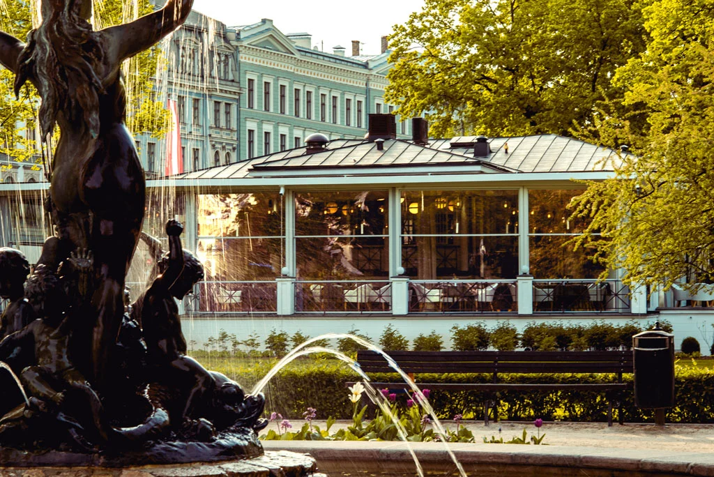 The Kolonāde glass pavilion in Riga seen across a park fountain