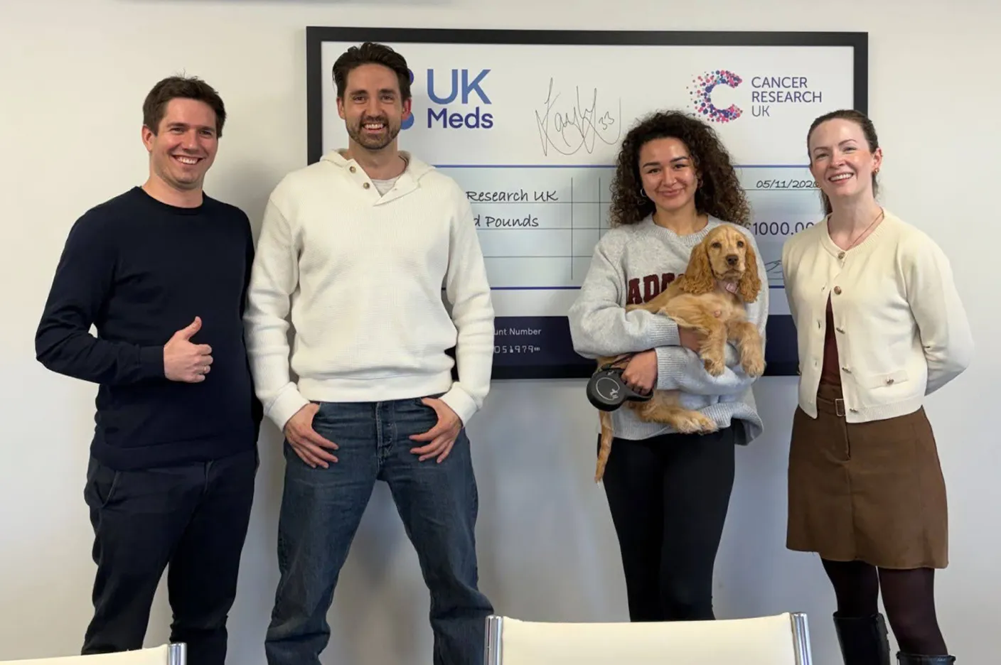Four people standing and smiling in front of a large Cancer Research UK check, one holds a dog.
