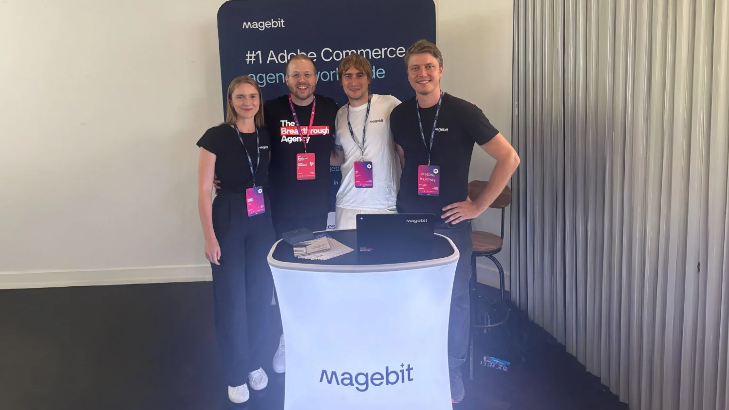 Four Magebit team members at the Meet Magento UK 2026 booth in front of the "#1 Adobe Commerce agency worldwide" banner