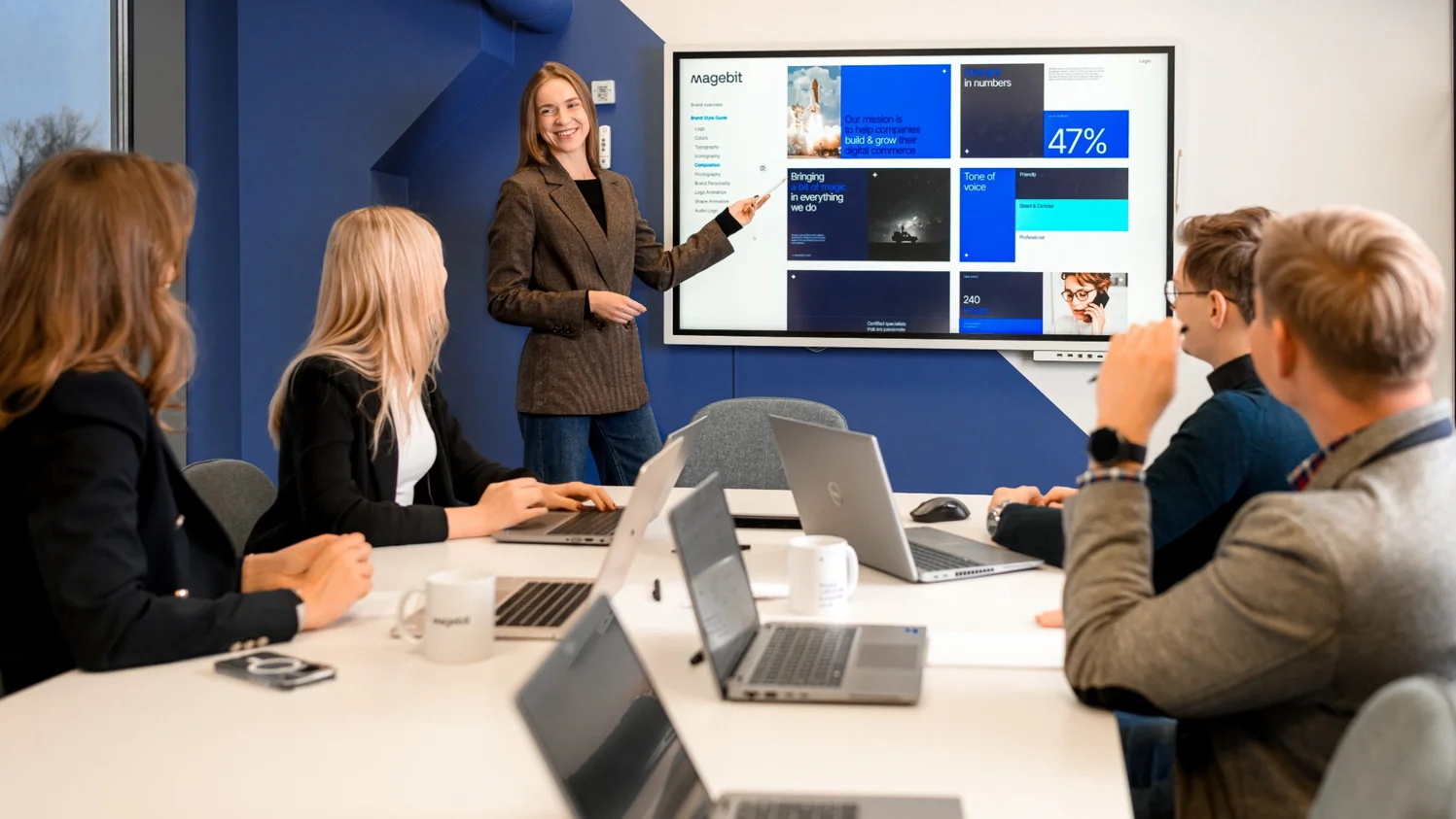 Magebit team members in a meeting at the company's headquarters office in Riga, Latvia, with a colleague presenting the Magebit brand guide on screen
