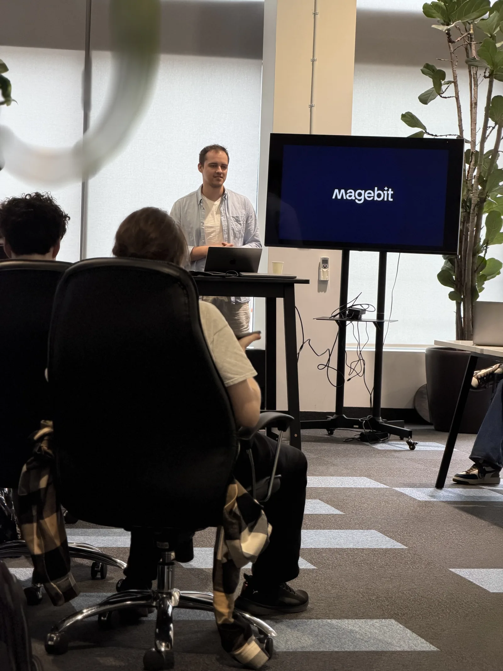 Bootcamp kick-off in the Magebit office, a speaker beside a Magebit-branded screen with participants at their desks