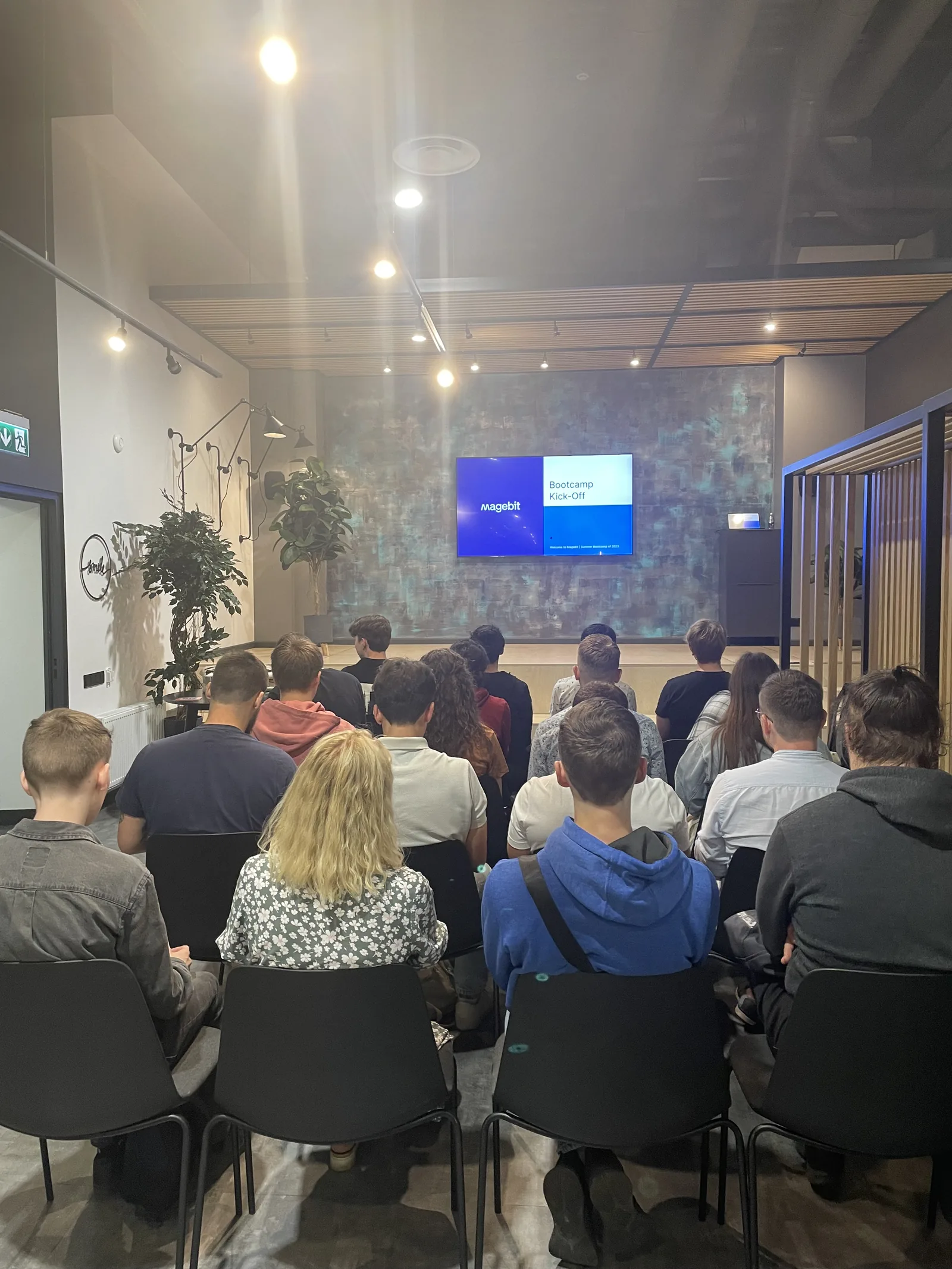 Participants seated in front of the "Bootcamp Kick-Off" slide on the Magebit office stage in Riga