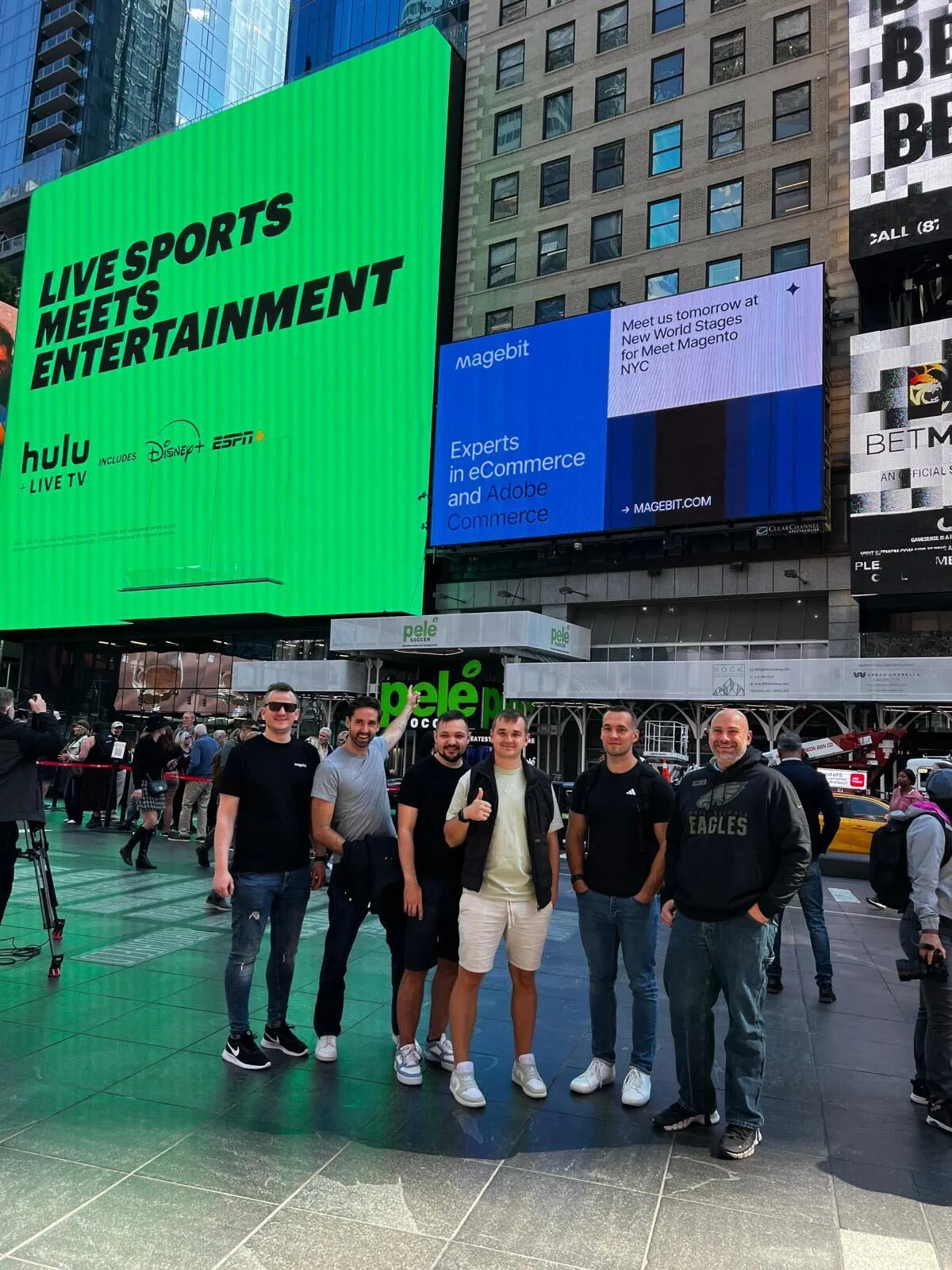 Magebit team in Times Square under a Magebit billboard announcing Meet Magento NYC at New World Stages