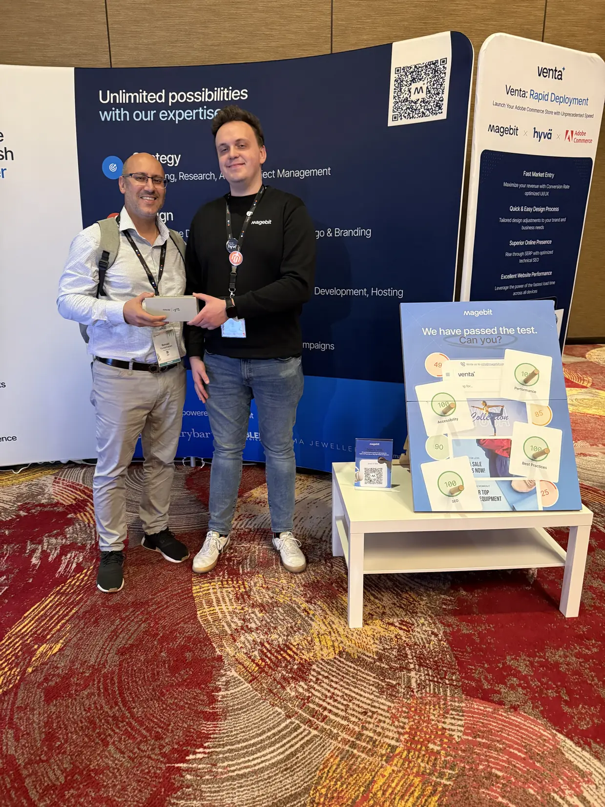 Two people at the Magebit booth at Meet Magento Florida 2025, with the Magebit and Venta backdrop behind them