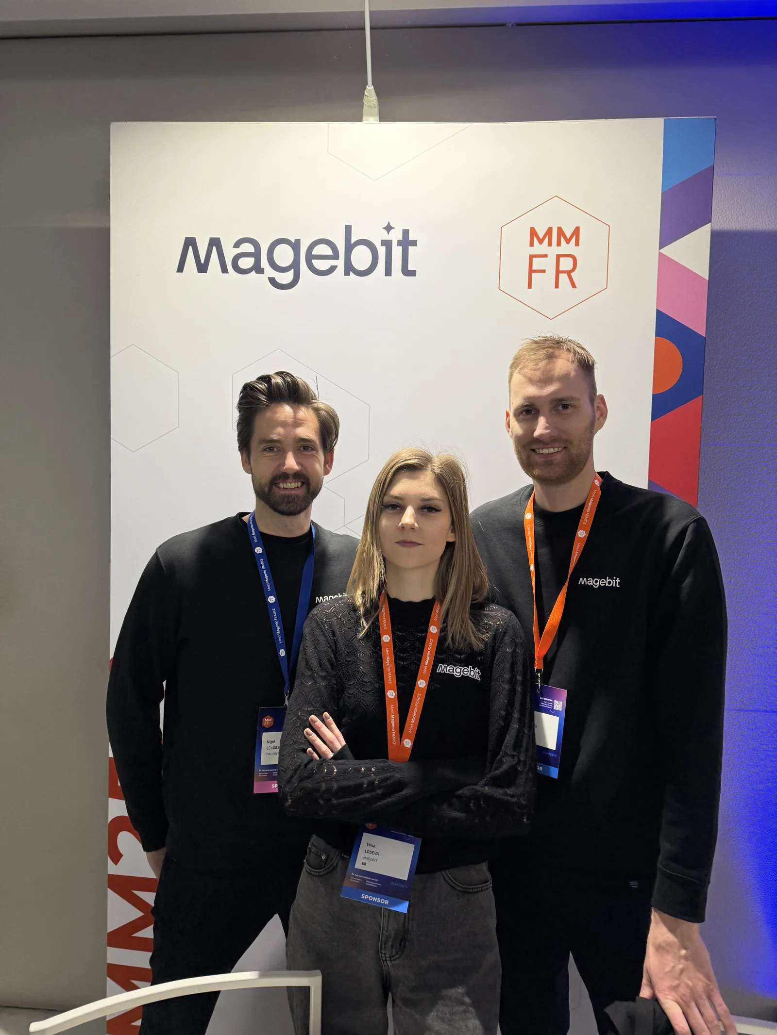 Three Magebit team members in front of the Magebit and Meet Magento France banner