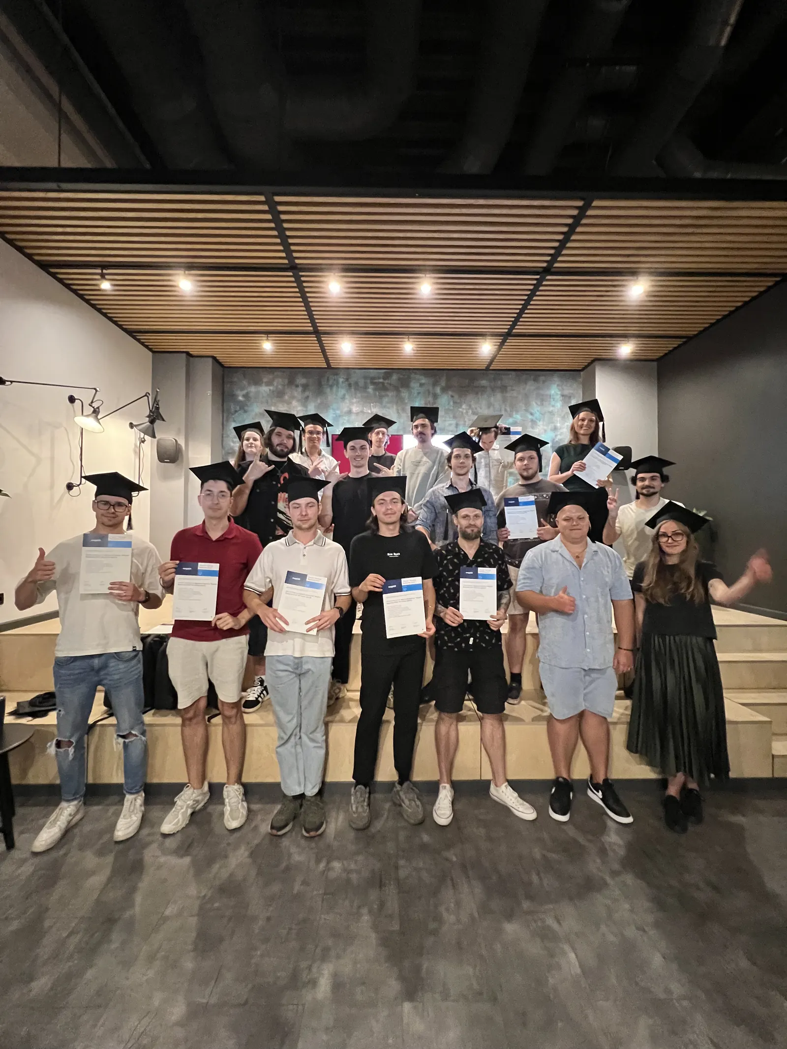 Magebit IT Bootcamp 2024 graduates in mortarboards holding their certificates on the Magebit office stage
