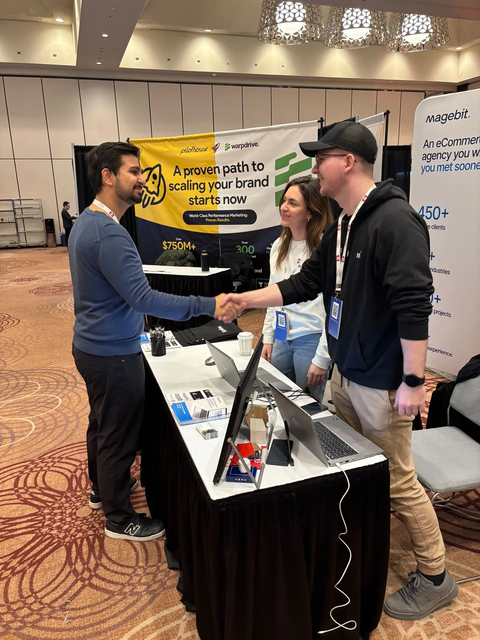 A Magebit team member shaking hands with a visitor across the booth table at DX3 Canada 2025