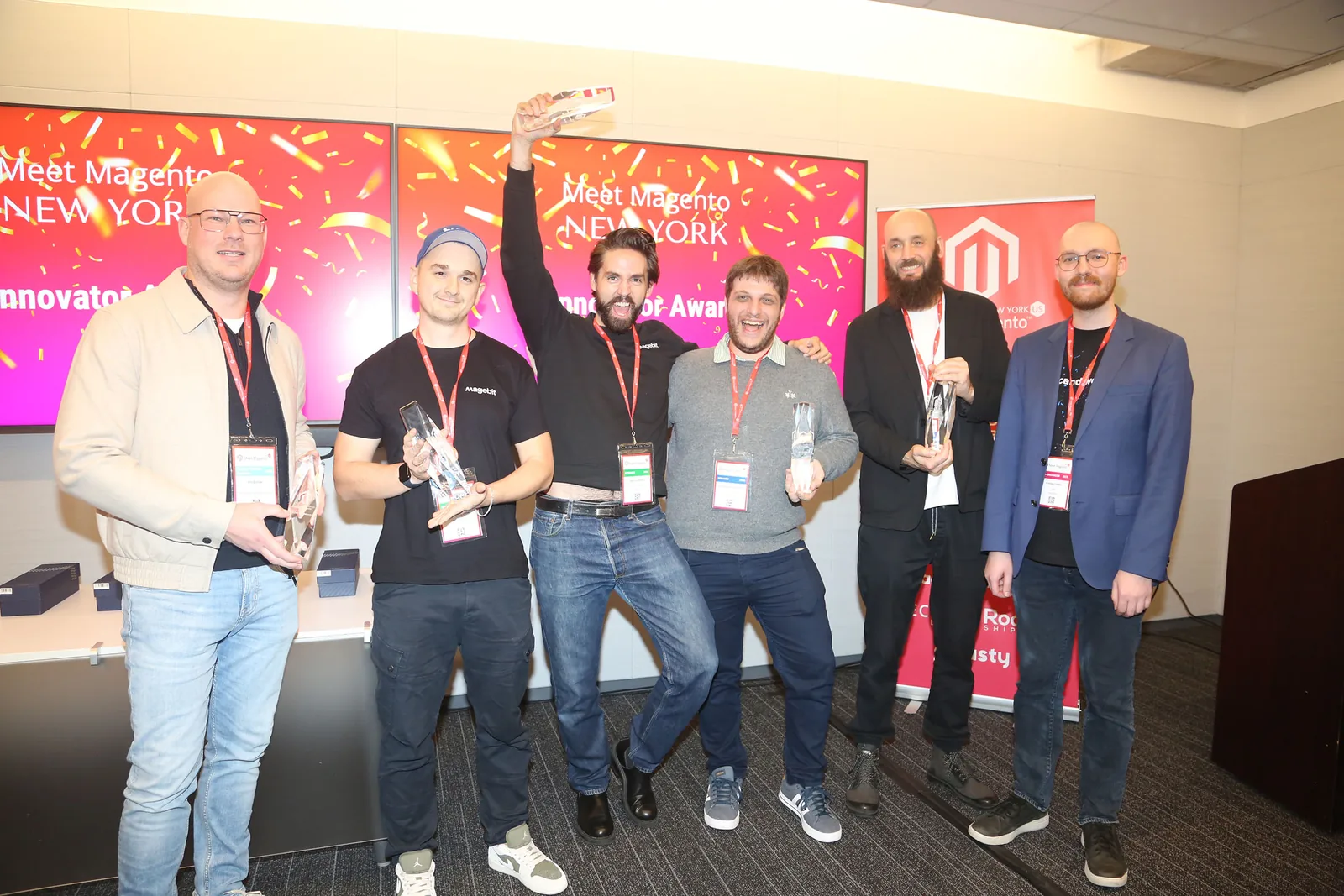 Award winners on stage at Meet Magento New York 2025, two Magebit team members holding trophies