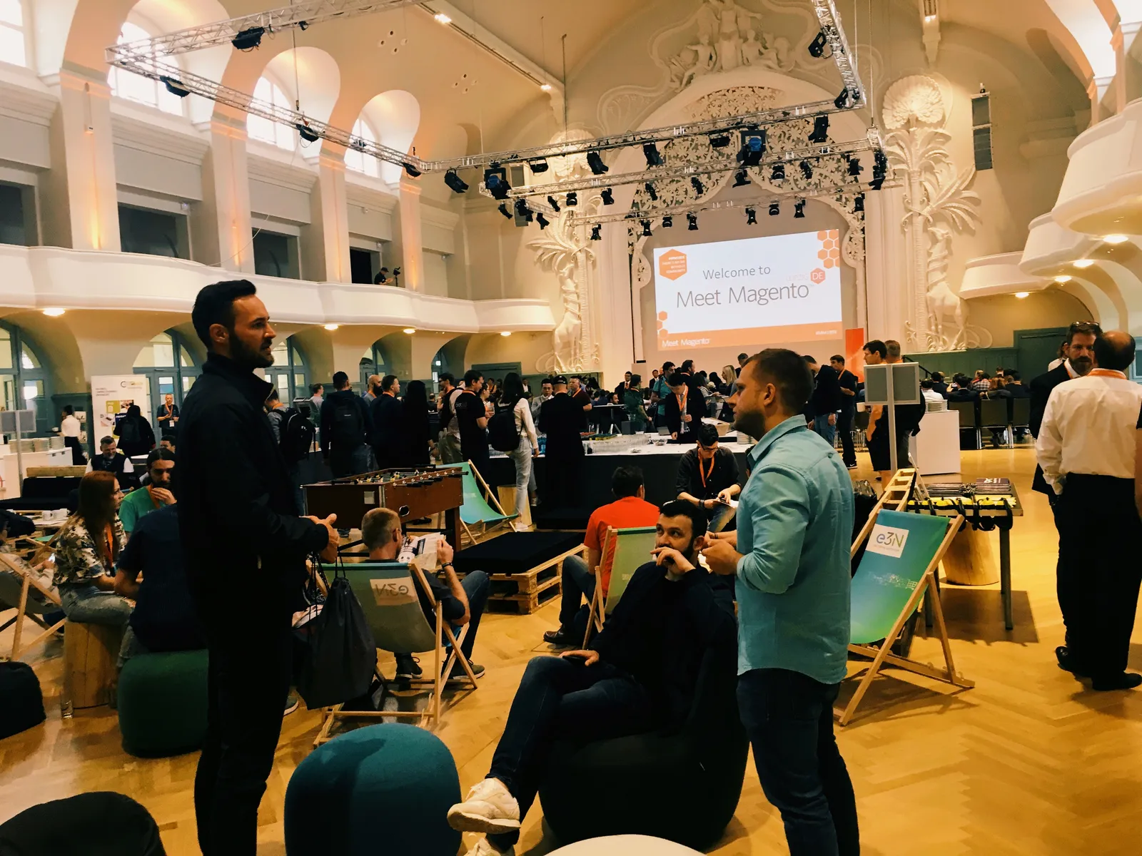 Attendees networking in the Kongresshalle am Zoo Leipzig, with the Welcome to Meet Magento screen on stage