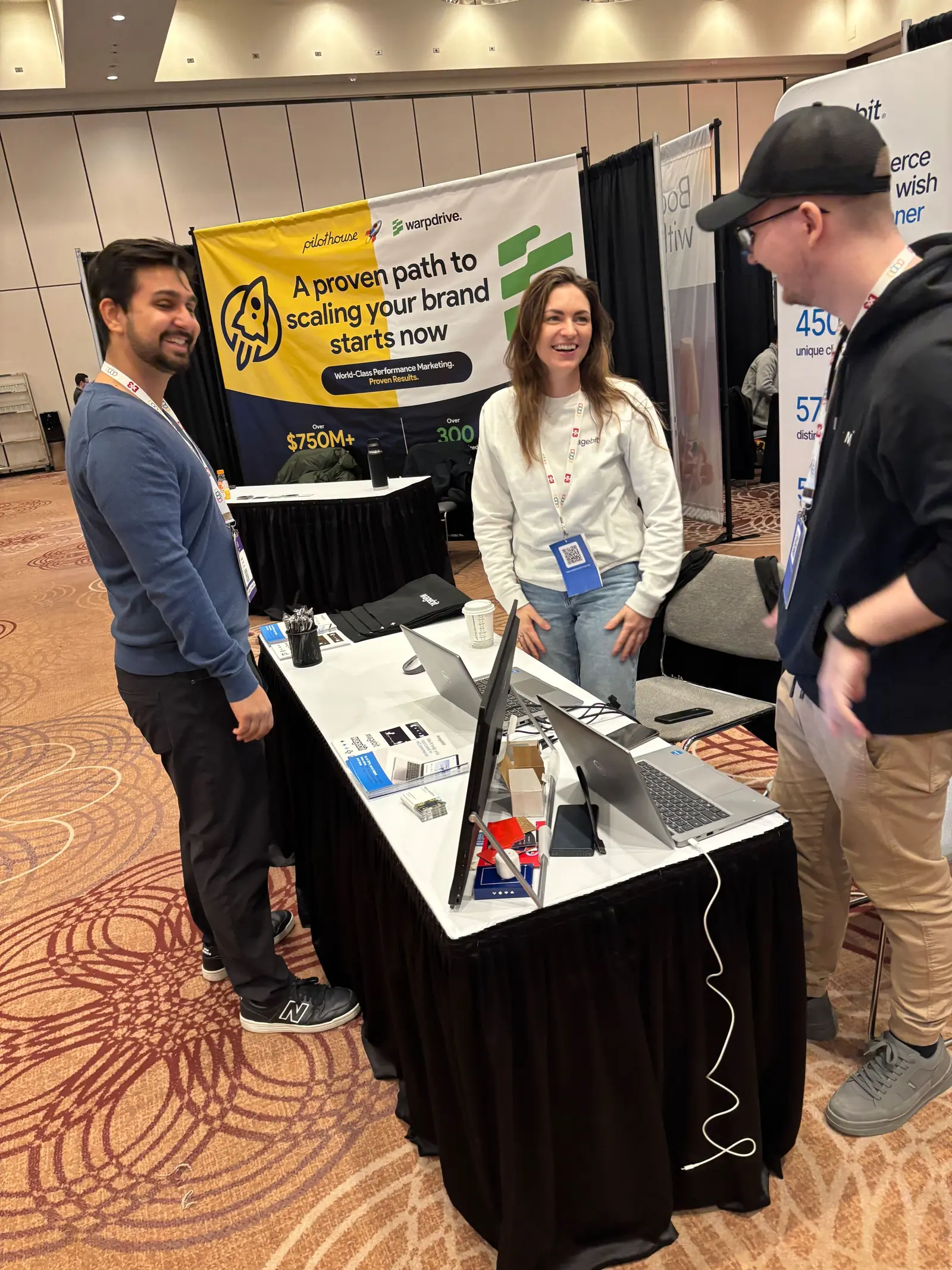 Two Magebit team members laughing with a visitor at the Magebit booth at DX3 Canada 2025