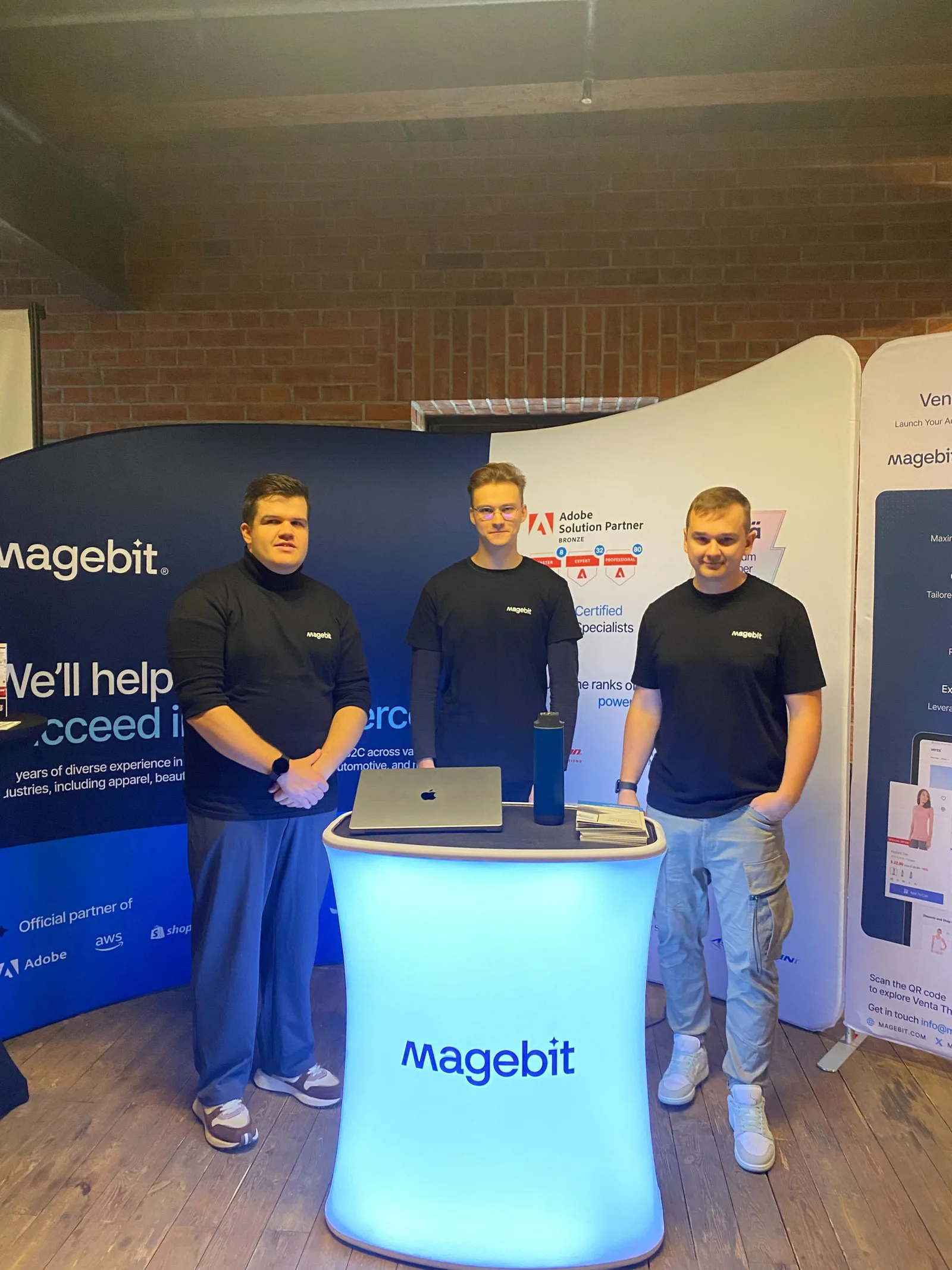 Three Magebit team members behind the illuminated Magebit counter at Meet Magento Poland 2024