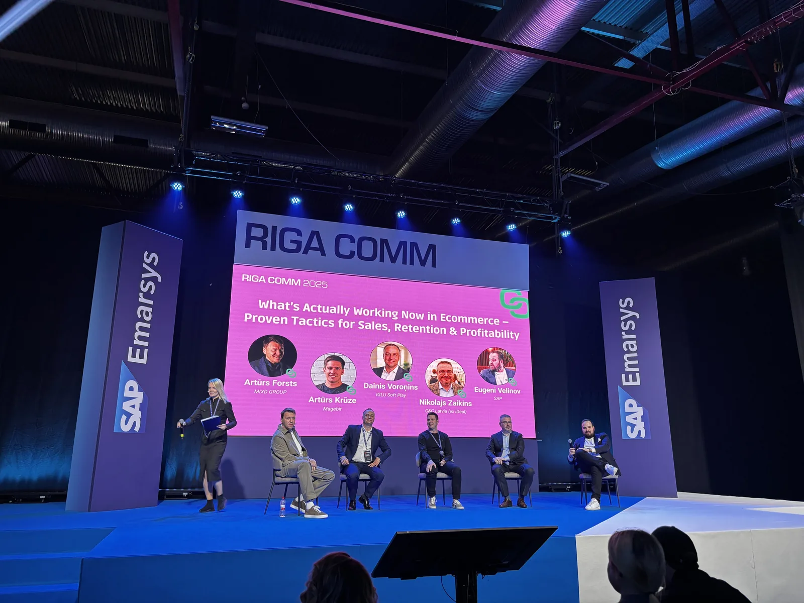 Moderator introducing the five e-commerce panellists from MIXD GROUP, Magebit, IGLU Soft Play, C&C Latvia and SAP at RIGA COMM 2025