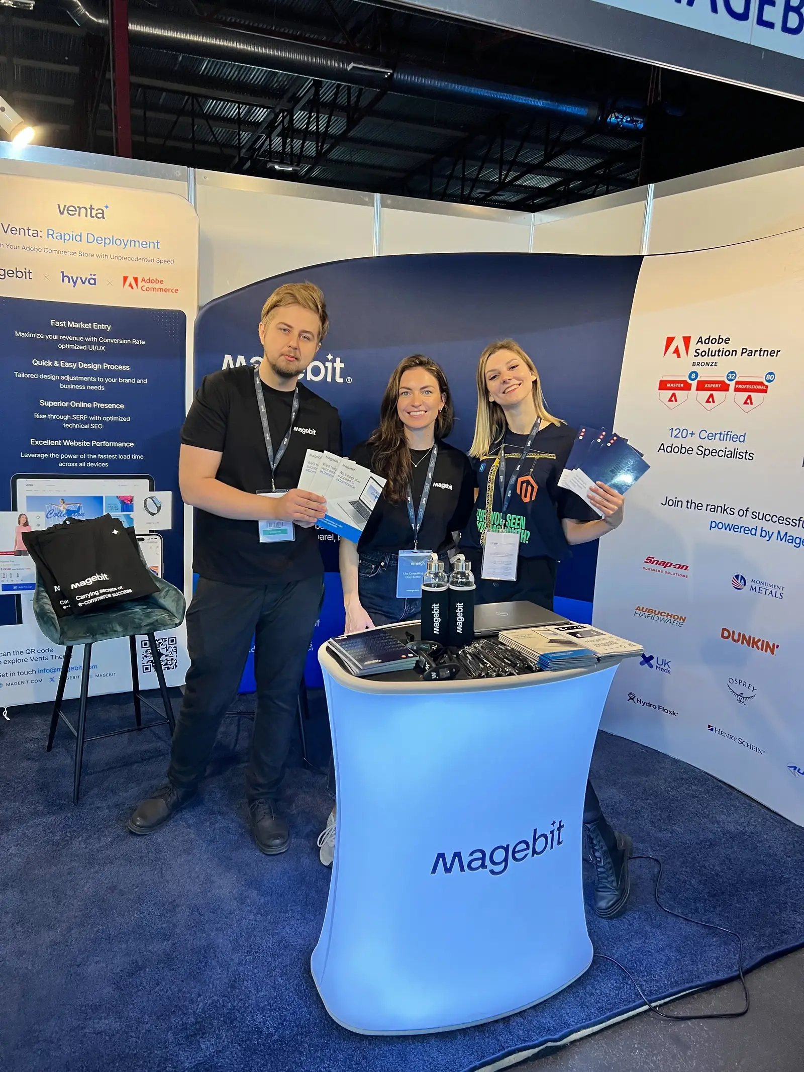 Magebit team holding brochures at the booth at RIGA COMM 2024