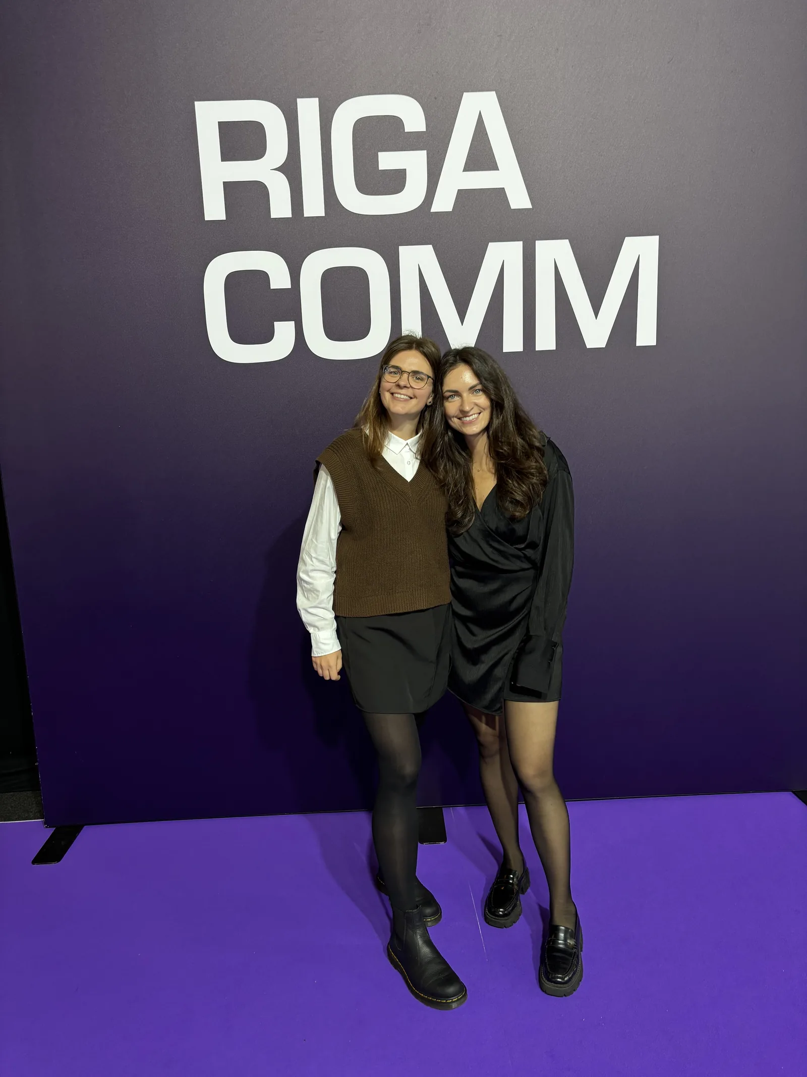 Two Magebit team members in front of the RIGA COMM sign