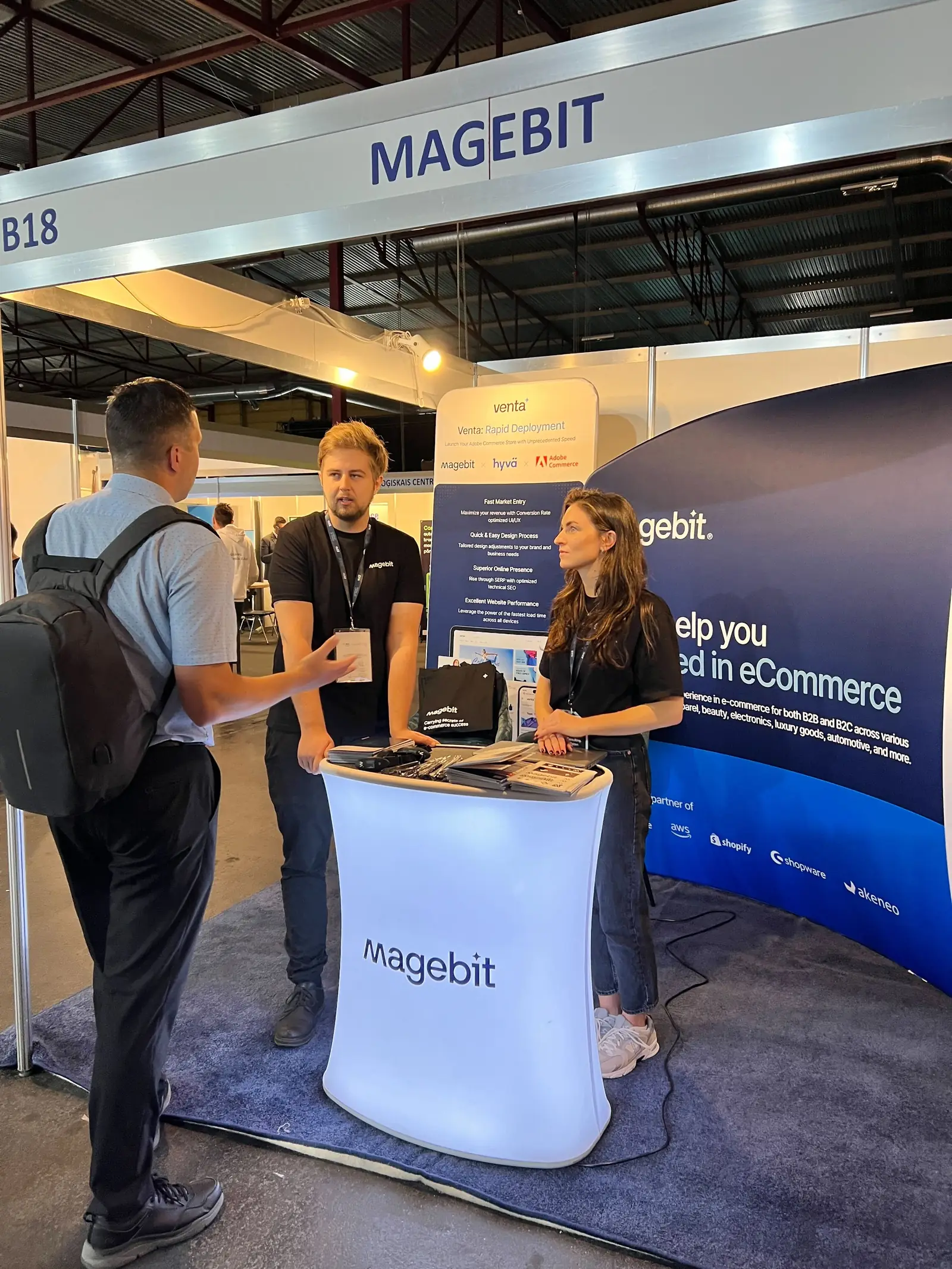 Magebit team talking with a visitor at stand B18 at RIGA COMM 2024