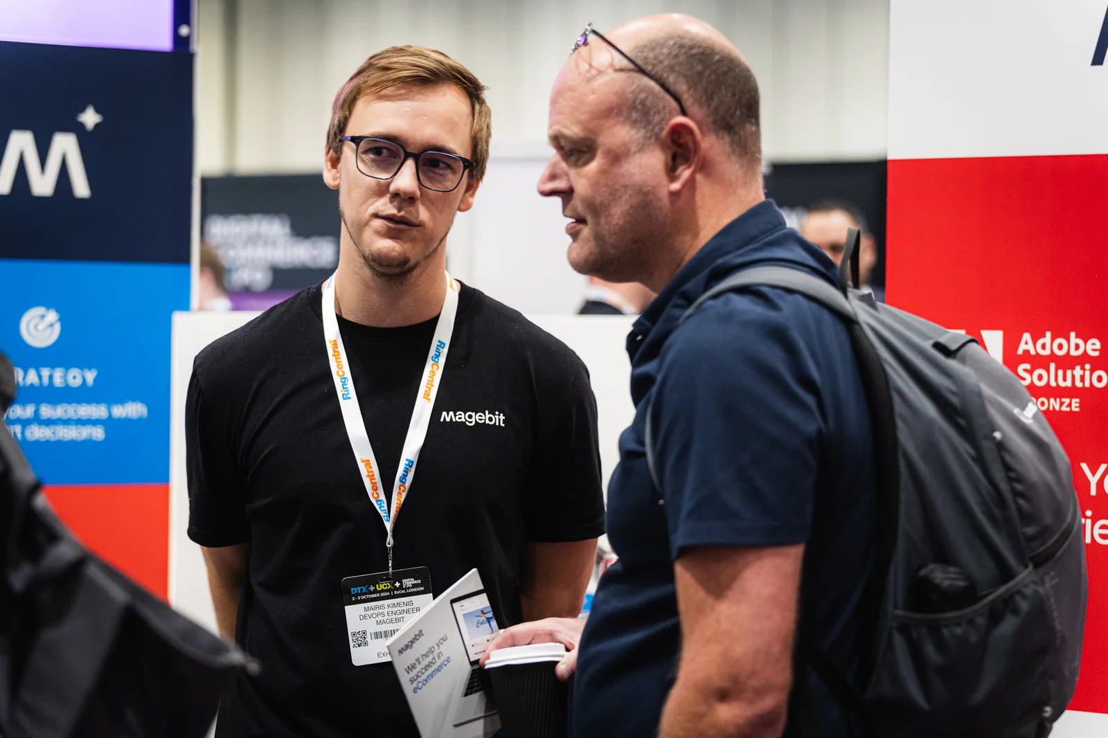 Magebit team member in discussion with a visitor beside the Adobe Solution Partner wall at Digital Commerce Expo 2024