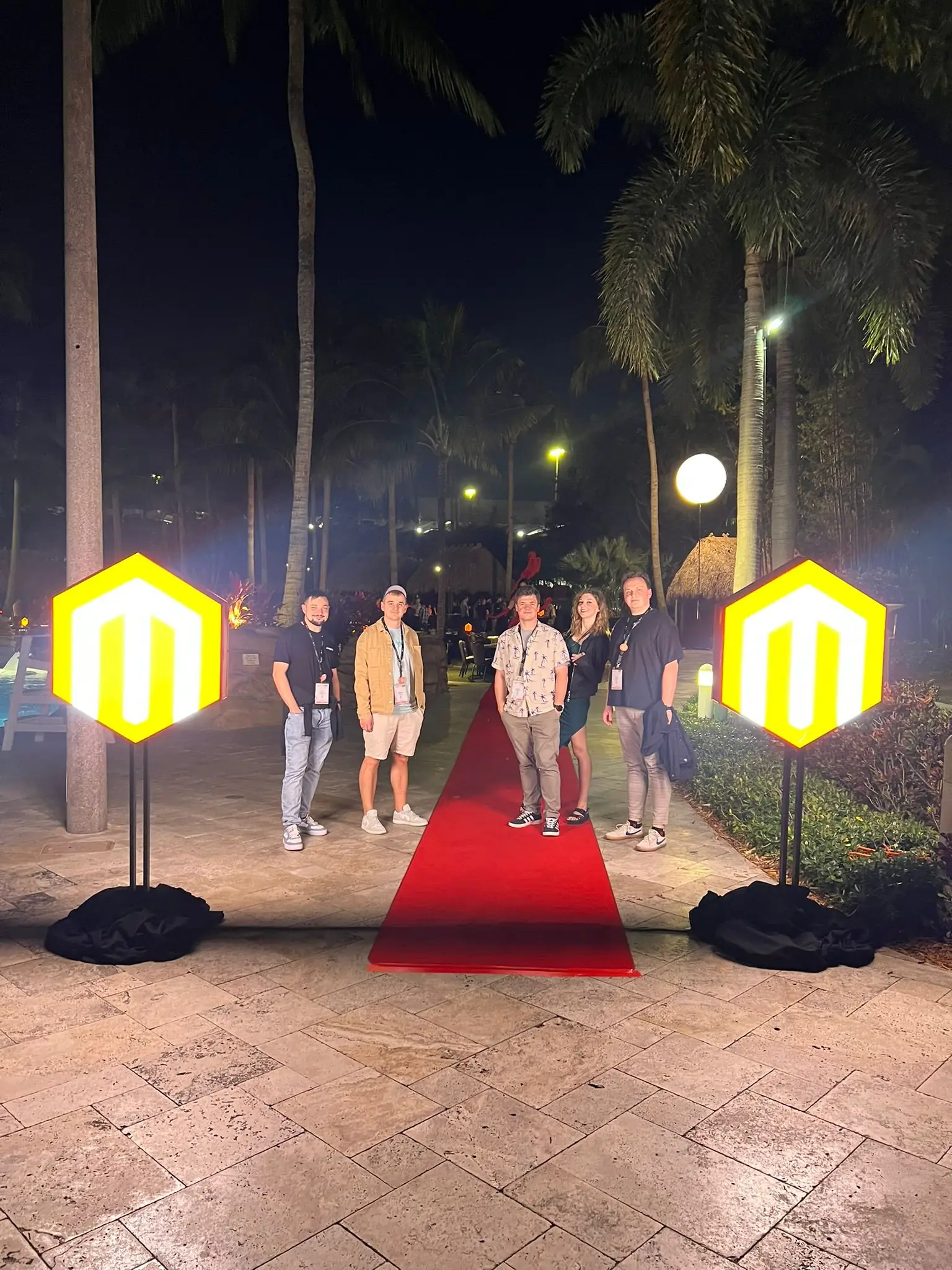 Magebit team on a red carpet between two illuminated Magento logos at the Meet Magento Florida 2025 evening event
