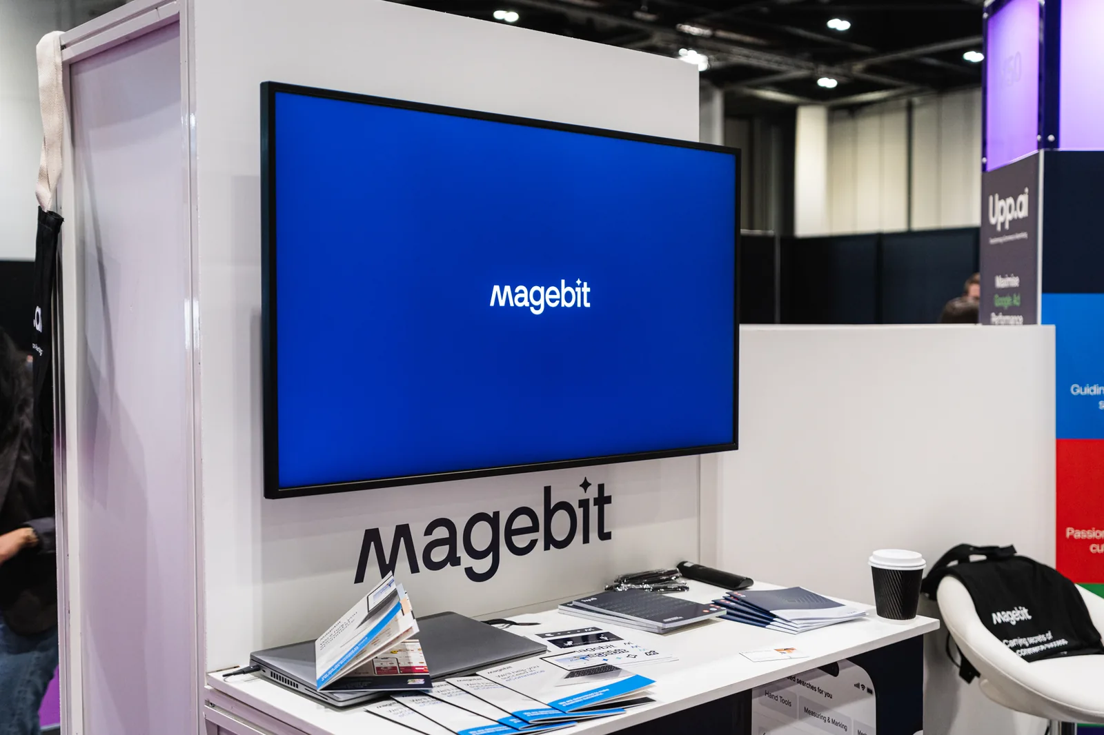 Magebit stand counter with brochures and a screen showing the Magebit logo at Digital Commerce Expo 2024