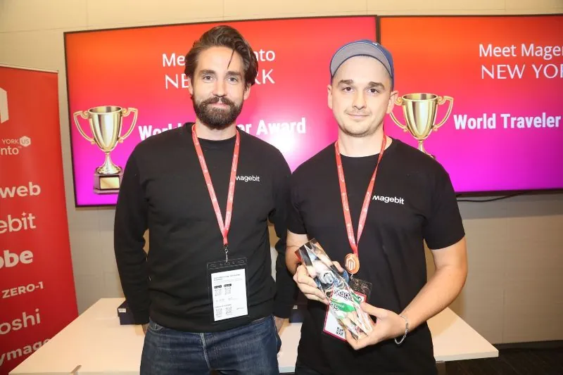 Artūrs Krūze and a Magebit teammate at Meet Magento NYC 2025, World Traveler Award displayed on screens behind them