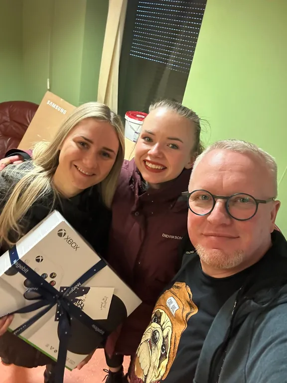 Edijs Klaišis with two Magebit visitors, holding a gifted Xbox, a Samsung TV box behind them