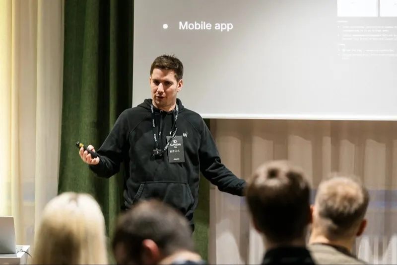 Artūrs Krūze presenting on stage at Cursor Meetup Riga, Magebit badge on his lanyard