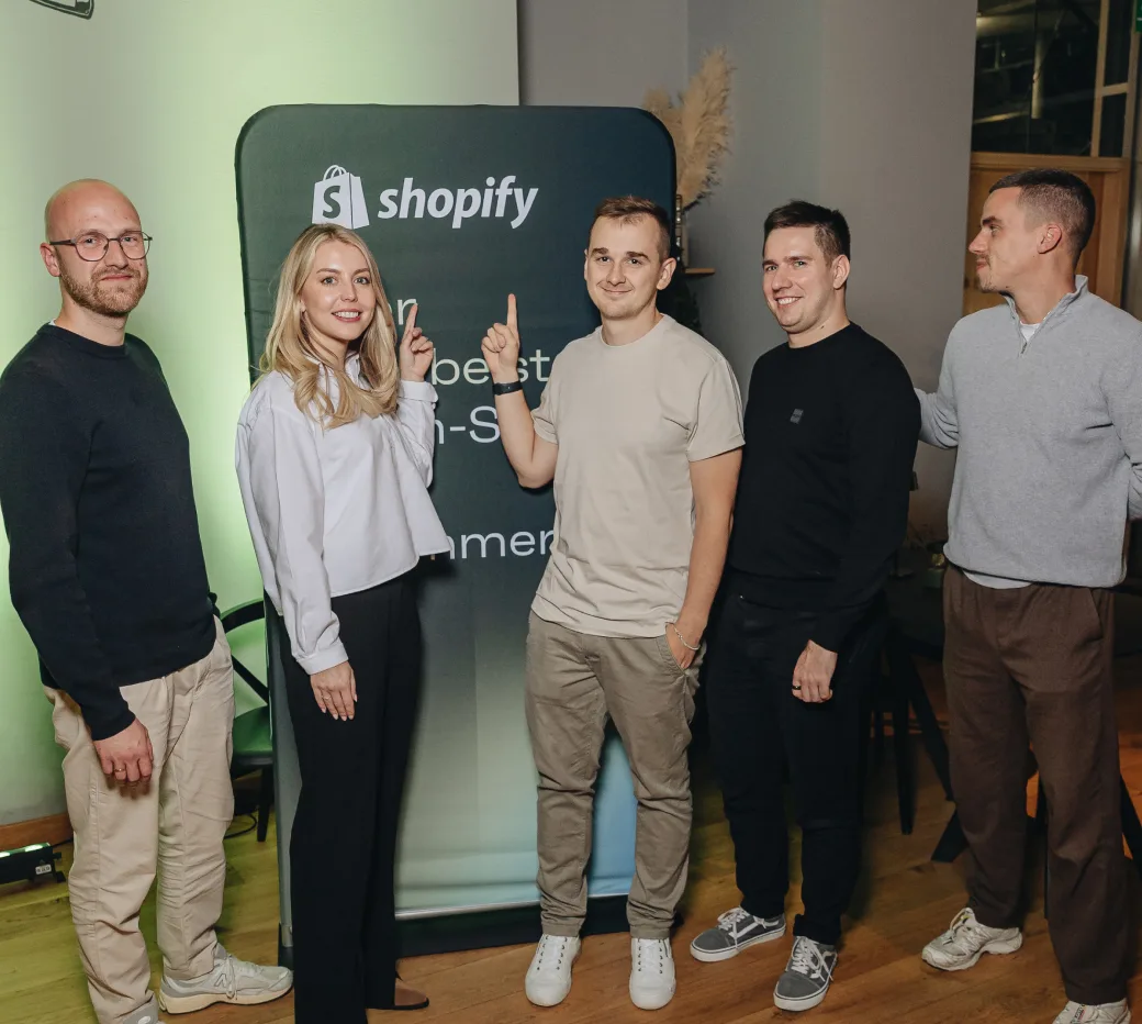 Five Magebit Shopify specialists standing in front of a Shopify banner